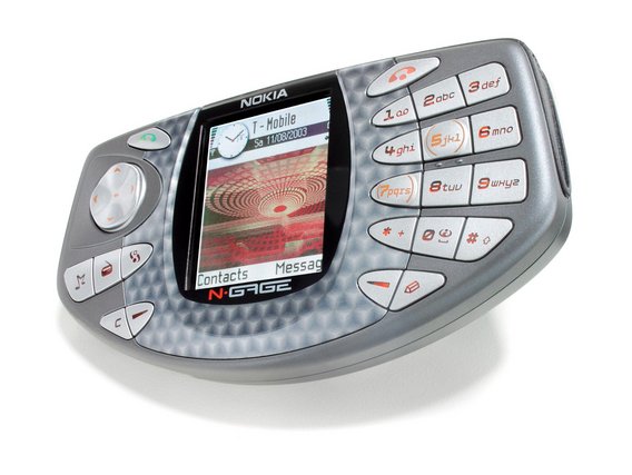 Ein Nokia N-Gage Gaming-Handy aus den frühen 2000ern mit silbernem Design und blau-kariertem Muster. Das Display zeigt das T-Mobile Interface mit Kontakten und Nachrichten-Menü.