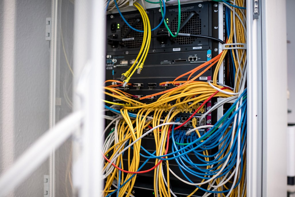 Netzwerk-Rack mit farbigen Kabeln (gelb, blau, grün, orange, weiß) und mehreren Servern mit blinkenden LEDs.
