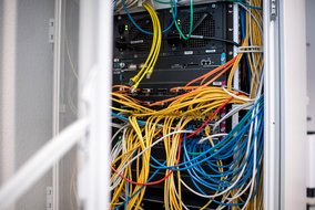 Netzwerk-Rack mit farbigen Kabeln (gelb, blau, grün, orange, weiß) und mehreren Servern mit blinkenden LEDs.