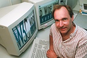 Tim Berners-Lee in gestreiftem Hemd sitzt vor einem Computer mit CRT-Monitor, auf dem "World Wide Web" zu lesen ist, typische 1990er Jahre Büroeinrichtung.