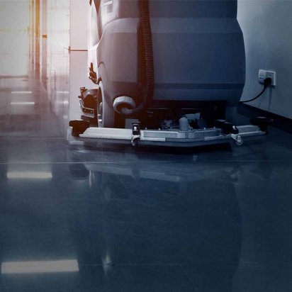 Eine professionelle Bodenreinigungsmaschine säubert einen glänzenden Fliesenboden in einem modernen Gebäude. Die Maschine ist in Betrieb und reflektiert das Licht der Umgebung, was auf eine gründliche Reinigung hinweist.