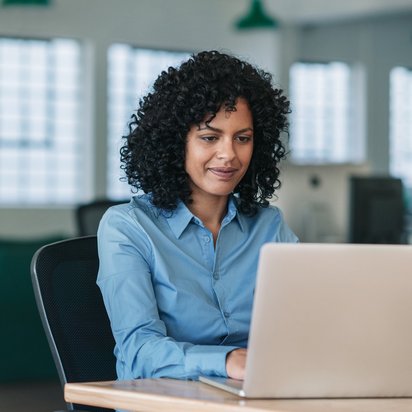 Personenzertifizierung Eine weibliche Person sitzt an einem Laptop und informiert sich über Personenzertifizierungen.