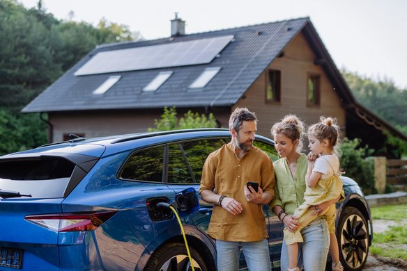 Familie lädt Elektroauto vor einem Haus mit Solaranlage