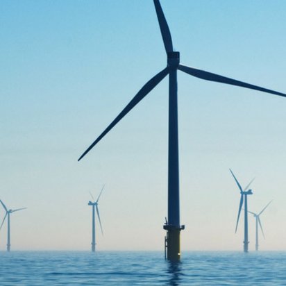 Ein Offshore-Windpark mit mehreren großen Windrädern, die aus dem blauen Meer ragen. Die Windturbinen erstrecken sich bis zum Horizont unter einem klaren, hellblauen Himmel.