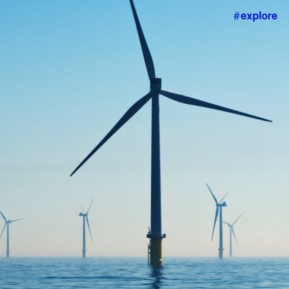 Ein Offshore-Windpark mit mehreren großen Windrädern, die aus dem blauen Meer ragen. Die Windturbinen erstrecken sich bis zum Horizont unter einem klaren, hellblauen Himmel.