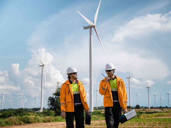 Zwei Techniker vor Windrädern mit Ausrüstung unterwegs