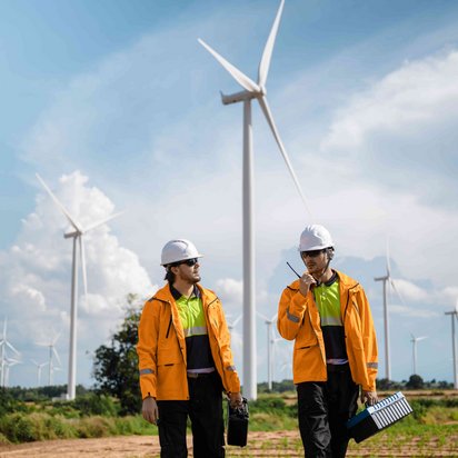 Zwei Techniker vor Windrädern mit Ausrüstung unterwegs