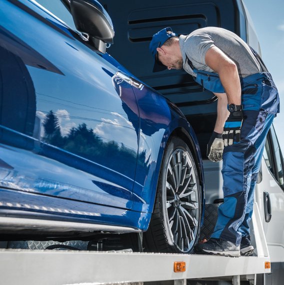Mitarbeitr inspiziert Fahrzeug auf Abschleppwagen