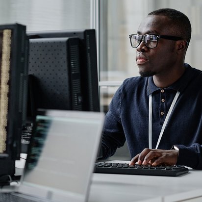 Person sitzt an einem Computerarbeitsplatz und arbeitet an mehreren Monitoren.