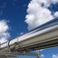 Im Vordergrund zu sehen ist eine silbern glänzende Pipeline, im Hintergrund blauer Himmel mit wenigen weißen Wolken.