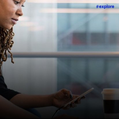 Eine Nahaufnahme einer Frau, die gleichzeitig mit ihrem Handy und Laptop arbeitet. Auf ihrem Schreibtisch steht eine Tasse Kaffee.