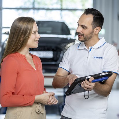 Ein Mitarbeiter des TÜV NORD erklärt einer Kundin im Autohaus die Details auf einem Tablet.