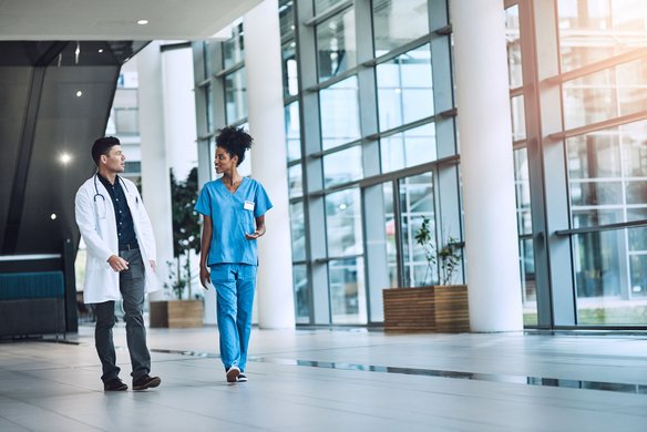 Zwei medizinische Fachkräfte gehen durch ein modernes Krankenhaus und unterhalten sich