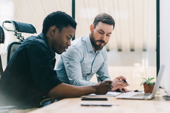 Zwei Männer arbeiten gemeinsam am Laptop in einem modernen Büro