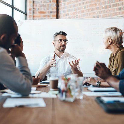 Eine Gruppe von Personen sitzt an einem Konferenztisch und diskutiert vor einem Whiteboard.