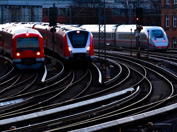 Mehrere Züge auf einem verzweigten Gleisnetz, Regionalzüge im Vordergrund, ICE im Hintergrund, urbaner Bereich.