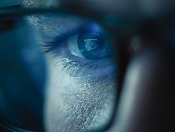 Nahaufnahme eines Brillenglases einer Person, die auf einem Monitor schaut