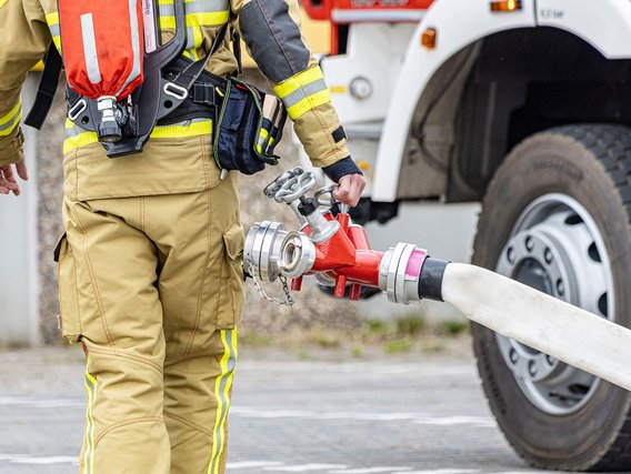 Feuerwehrmann mit Schlauch vor einem Feuerwehrauto