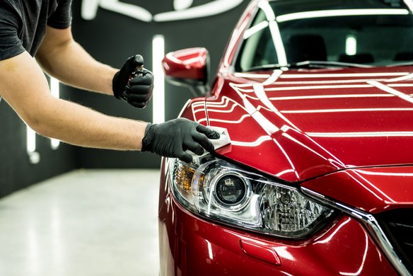 Rotes Auto von vorne und nur zur Hälfte, jemand putzt die Scheinwerfer