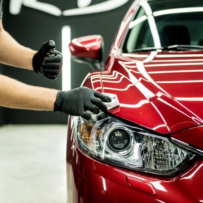 Rotes Auto von vorne und nur zur Hälfte, jemand putzt die Scheinwerfer