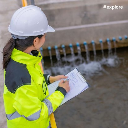 Ingenieurin mit weißem Helm und gelber Sicherheitsweste macht Notizen auf einem Klemmbrett vor einer Wasseraufbereitungsanlage mit Betonbecken.