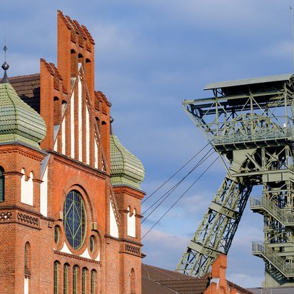 Backsteingebäude mit Zwiebeltürmen und Förderturm einer alten Zeche bei blauem Himmel