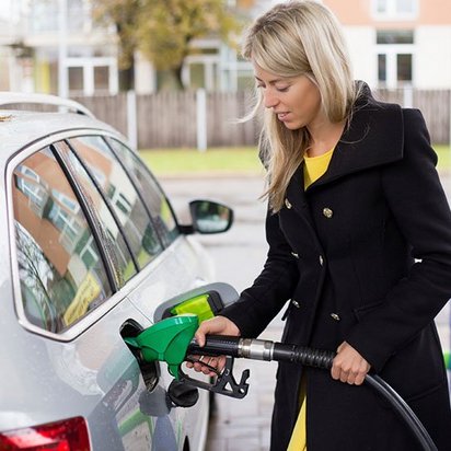 TÜV NORD Tankstellen und Tankläger Eine blonde Frau mit dunkler Jacke steht neben einem silbernen Auto und tankt.