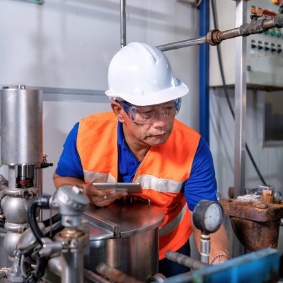 Techniker mit Schutzhelm und Warnweste inspiziert industrielle Rohrleitungen und Anlagenkomponenten
