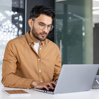 Datenschutzhinweise der TÜV NORD Akademie Mann mit Brille tippt an einem Laptop in einem modernen Büro