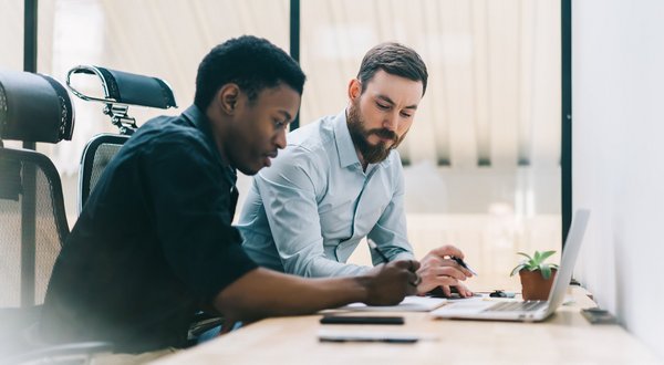 Zwei Männer arbeiten gemeinsam am Laptop in einem modernen Büro