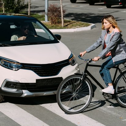 Bremsweg und Anhalteweg berechnen Frau fährt mit dem Fahrrad über einen Zebrastreifen und ein weißes Auto hält davor an