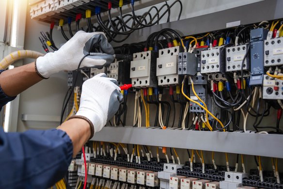 Elektriker misst mit einem Stromzangenmessgerät den Stromfluss in einer Schalttafel.