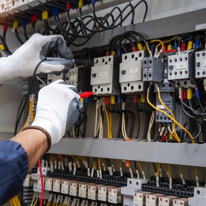 Elektriker misst mit einem Stromzangenmessgerät den Stromfluss in einer Schalttafel.