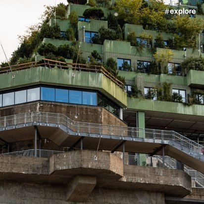 Ein hohes Gebäude mit begrünten Terrassen und Betonstrukturen unter einem bewölkten Himmel.