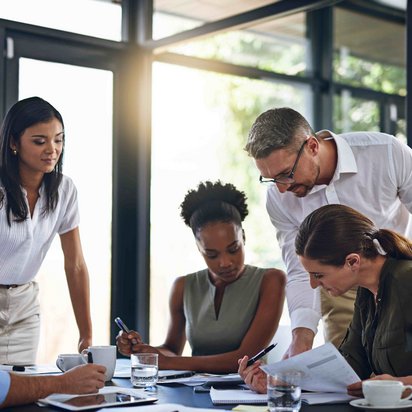 Gruppe von Menschen bei einer Besprechung in einem modernen Büro mit großen Fenstern.