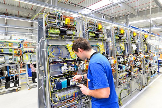  Techniker in blauer Kleidung arbeitet an einer industriellen Schalttafel in einer Fertigungshalle.