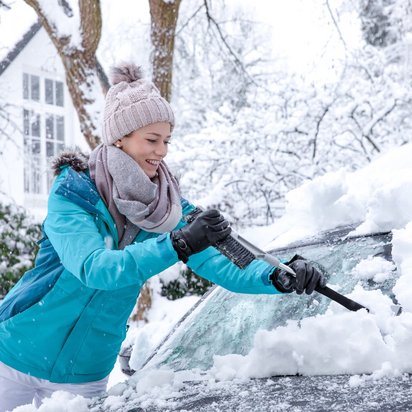 Schneeräumung am Auto im Winter Person in Winterkleidung räumt Schnee von einem Auto in einer verschneiten Umgebung.