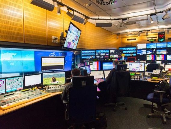 Kontrollraum mit mehreren Bildschirmen und Monitoren, auf denen verschiedene Inhalte angezeigt werden, wahrscheinlich eine Fernsehregie oder Überwachungszentrale.