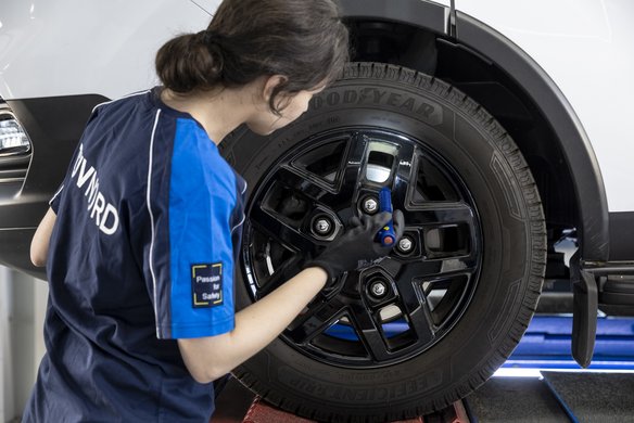 Frau mit einem blauen T-Shirt und der Aufschrift TÜV NORD steht an einem Rad und prüft etwas