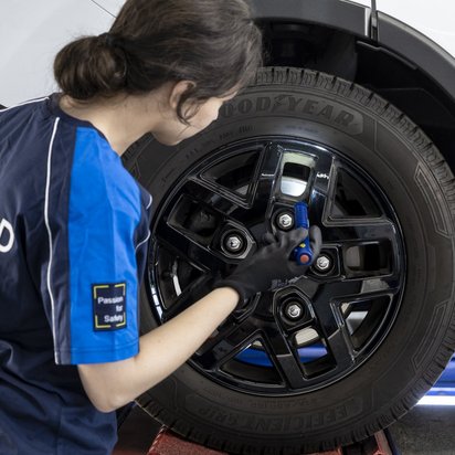 Frau mit einem blauen T-Shirt und der Aufschrift TÜV NORD steht an einem Rad und prüft etwas