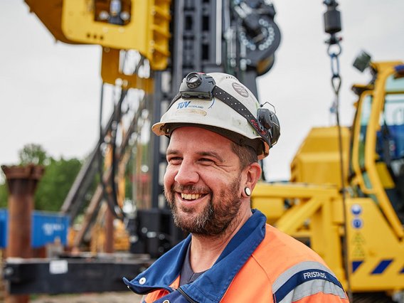 TÜV NORD-Krane Lächelnder TÜV NORD-Mitarbeiter mit Schutzhelm und Warnkleidung auf einer Baustelle.