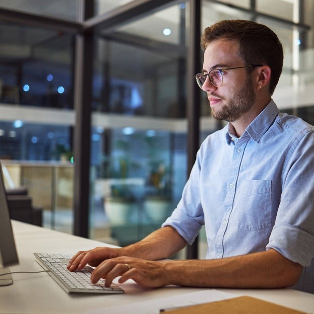 Ein KI-Spezialist (TÜV) sitzt vor seinem Computer-Arbeitsplatz in seinem Büro.