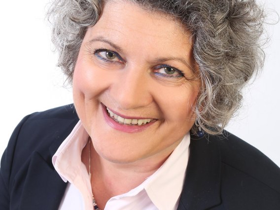 Dagmar Hildebrandt grauen, lockigen Haaren in einem dunklen Blazer und weißer Bluse lächelt in die Kamera.