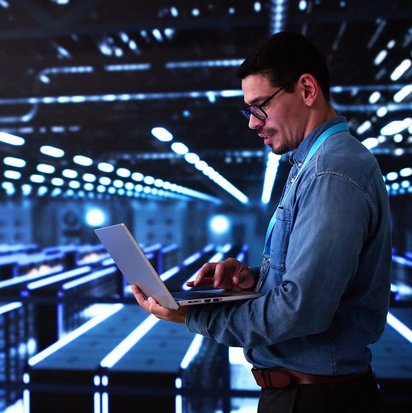 IT-Spezialist arbeitet mit Laptop in einem modernen, blau beleuchteten Serverraum.
