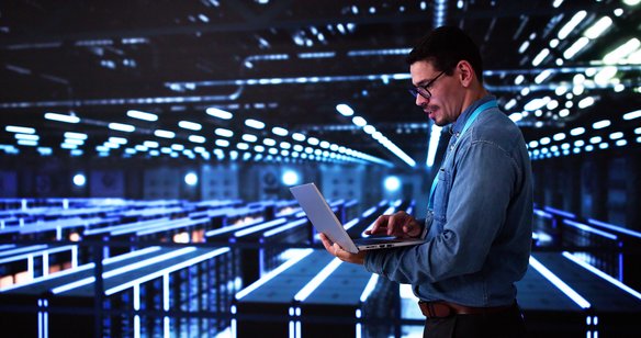 IT-Spezialist arbeitet mit Laptop in einem modernen, blau beleuchteten Serverraum.