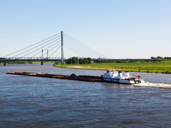 Frachtschiff auf dem Rhein bei Wesel mit Blick auf die Rheinbrücke und grüne Uferlandschaft