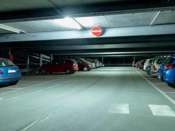 Eine Tiefgarage mit geparkten Autos auf beiden Seiten und freien Stellplätzen in der Mitte. Ein rundes rotes Verbotsschild ist an der Decke angebracht und die Garage ist mit Leuchtstoffröhren beleuchtet.