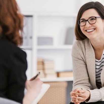 Lächelnde Frau in einem Gespräch mit einer anderen Person, die notiert