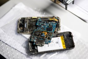 Geöffnetes Smartphone mit freiliegender Platine und Batterie auf einer weißen Unterlage, vermutlich während einer Reparatur.
