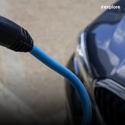 Nahaufnahme eines blauen Ladekabels, das ein Elektrofahrzeug mit einem BMW-Logo an der Seite lädt.